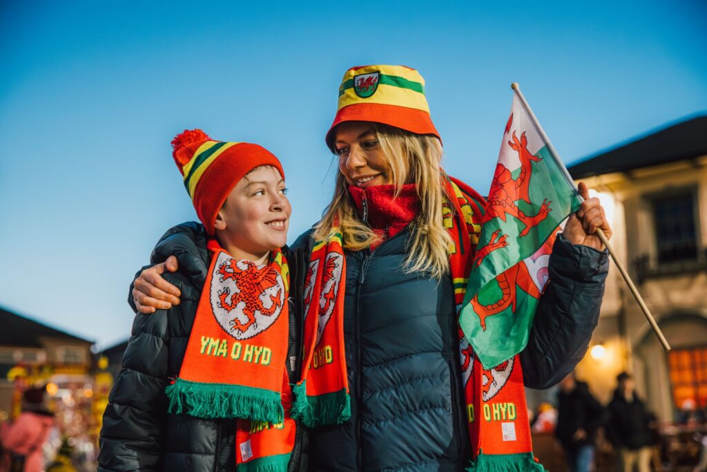 Mother and son dressed in Welsh hats and scarves with flag for football match