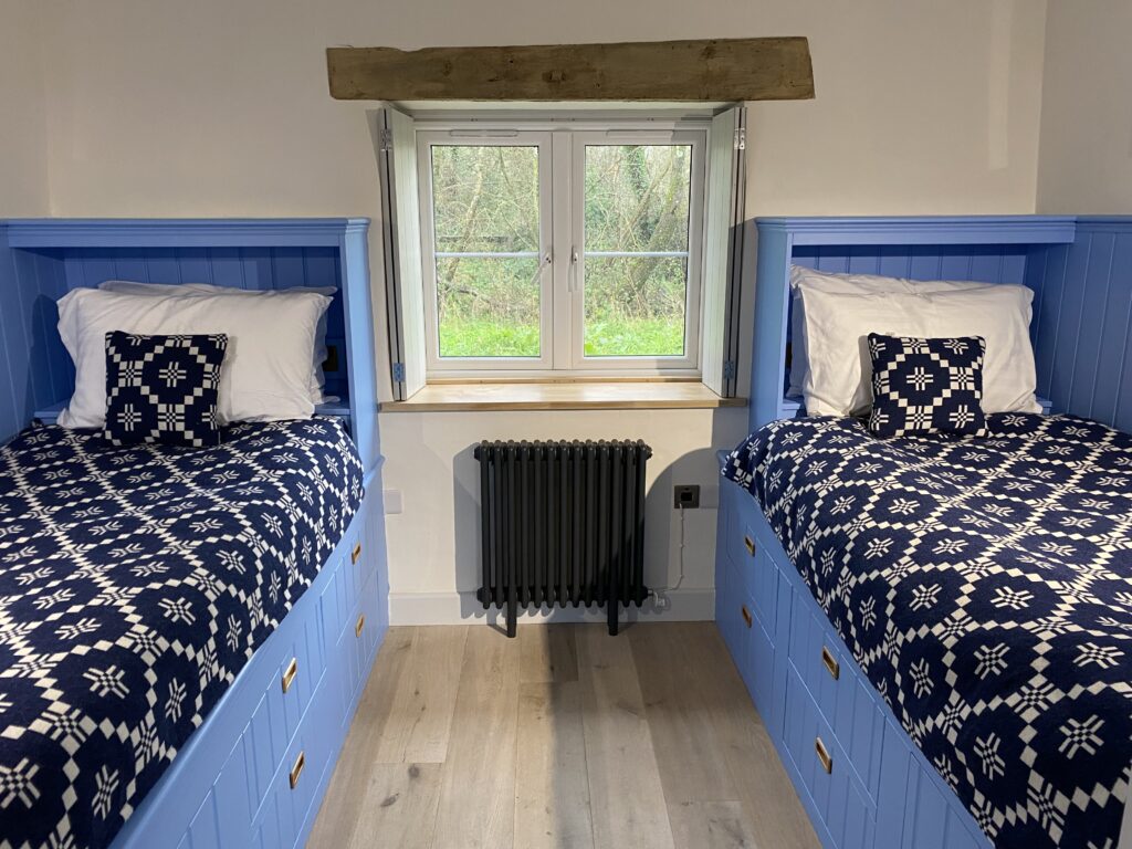 Twin cabin beds in cottage with blue bed frames with drawers and dark blue patterned Welsh wool blankets