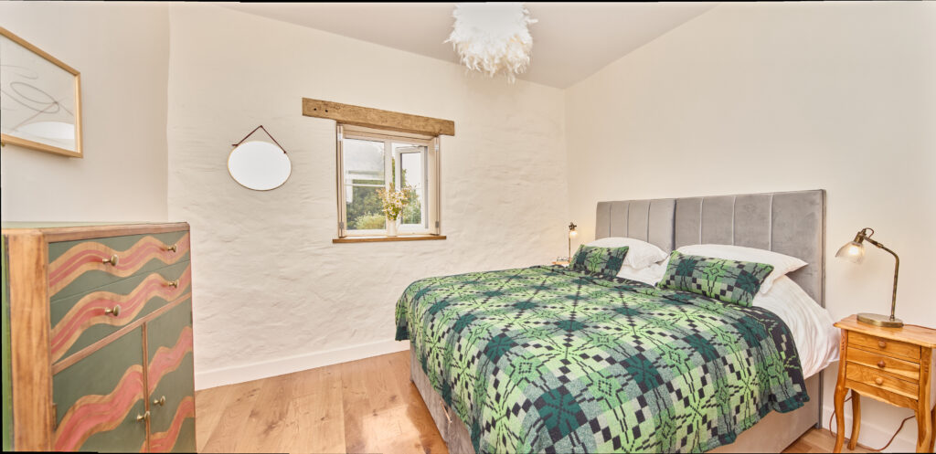 Bedroom in cottage with large bed with green patterned Welsh wool blanket on bed