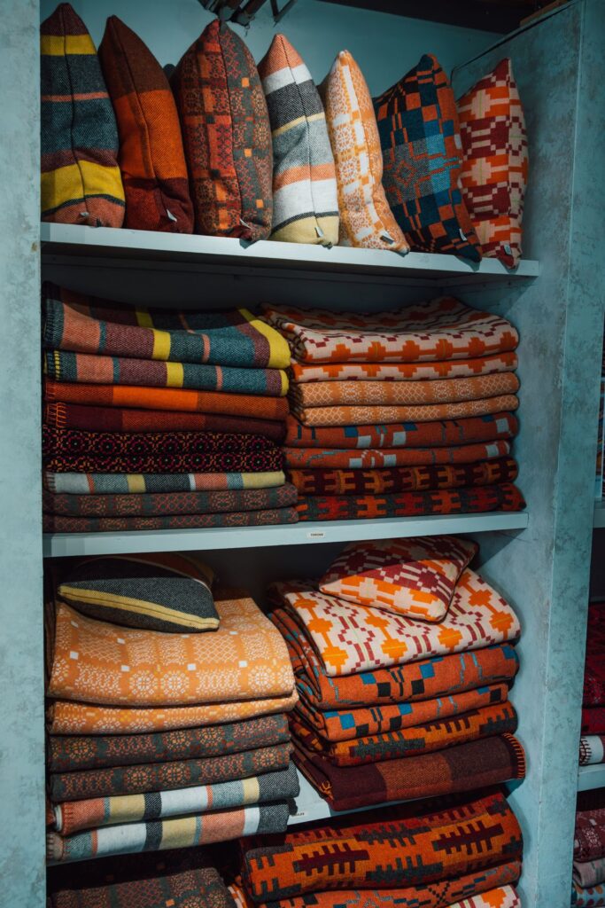 Orange and red Welsh wool blankets and cushions on shelves in Melin Tregwynt shop
