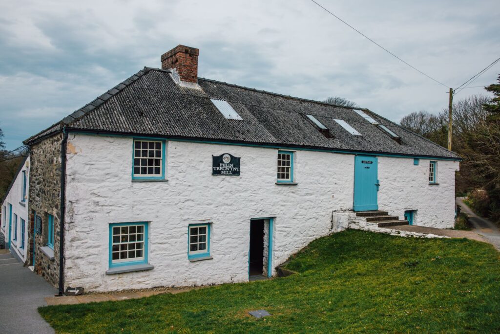 Outside of Melin Tregwynt building, painted white with blue door and windows and grassy bank